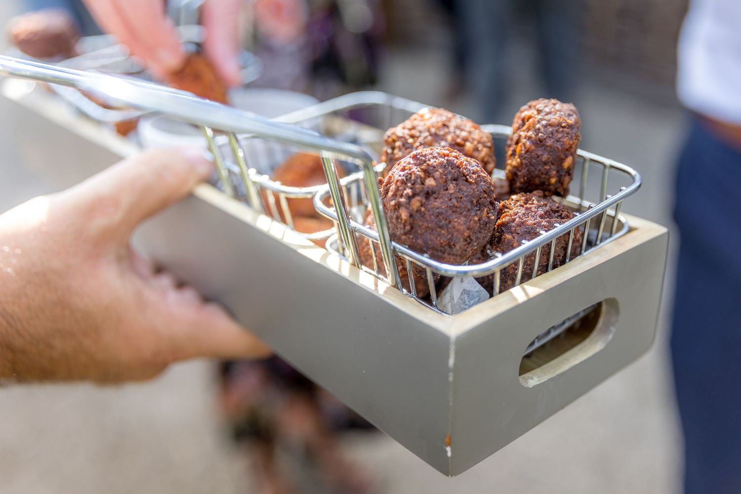 Catering staff serving appetizers on white trays at an outdoor event.