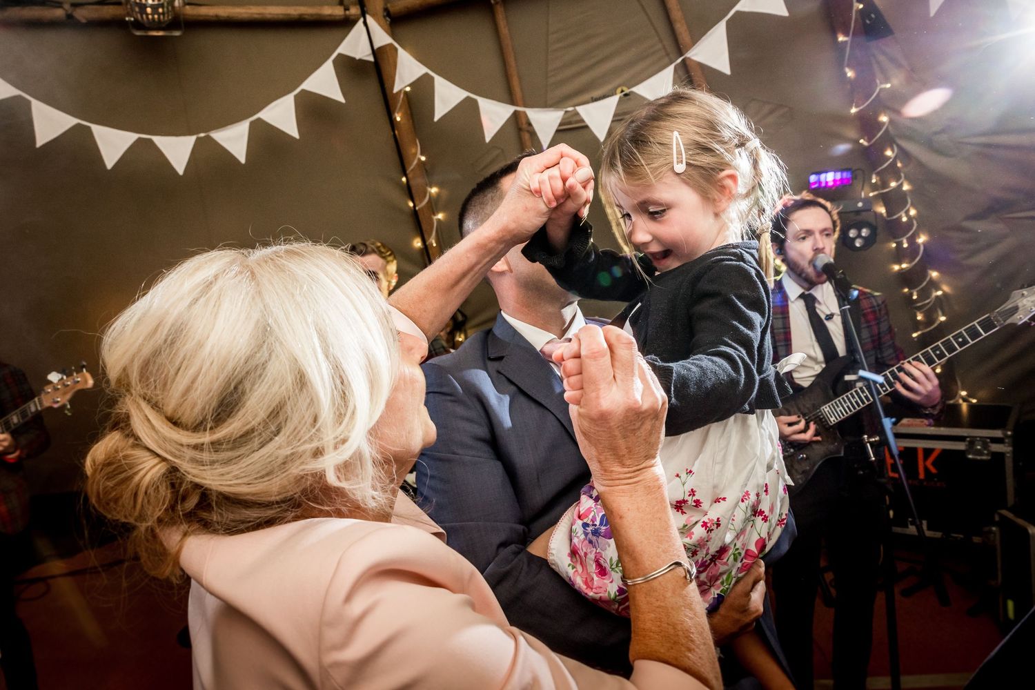 A child dances with guests during a wedding reception while the band performs in the background.