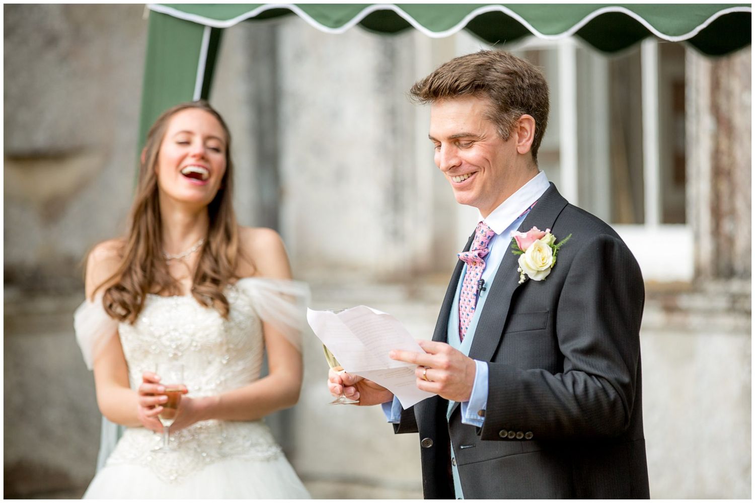 A bride and groom share a joyful moment while reading papers during their outdoor wedding ceremony.