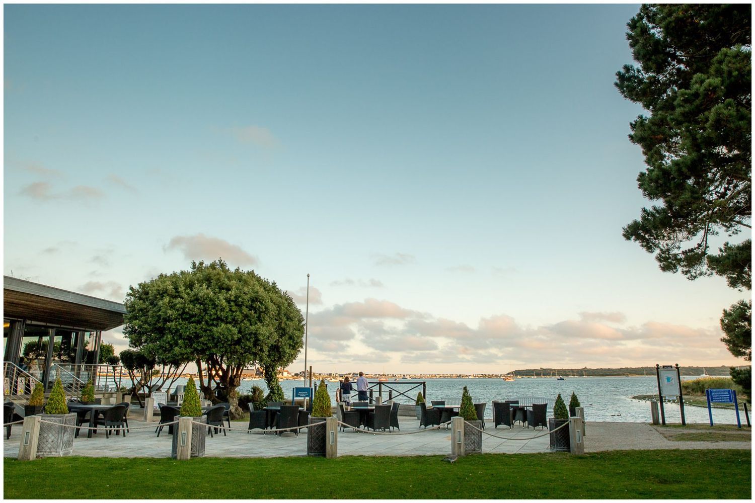 A panoramic sequence of seven photos showing a peaceful waterfront park with benches, trees, and ocean views at sunset.