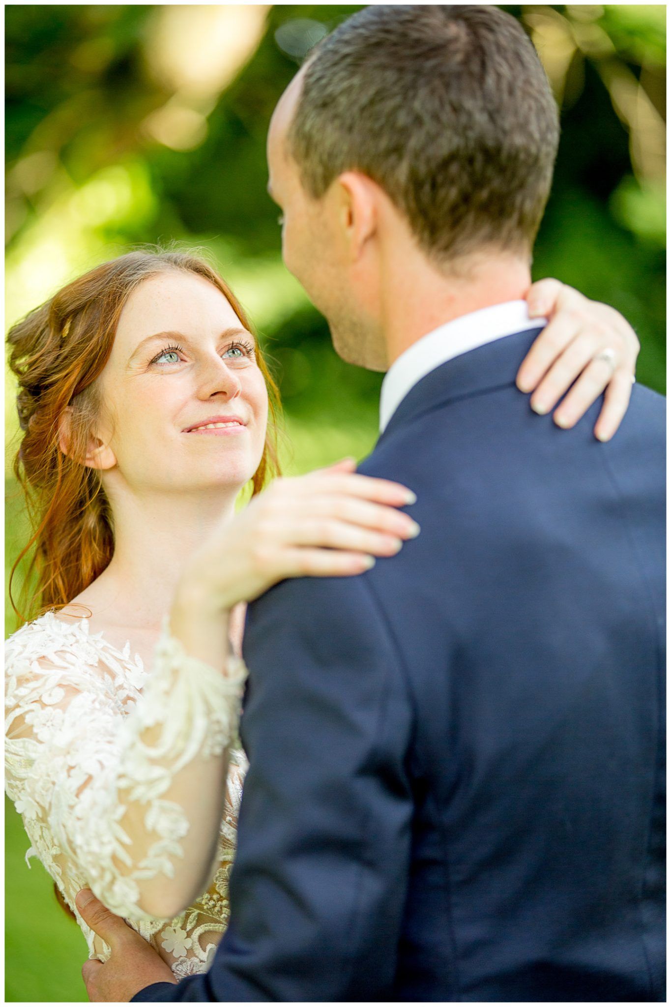 A tender moment between newlyweds embracing outdoors, with soft sunlight filtering through greenery in the background.