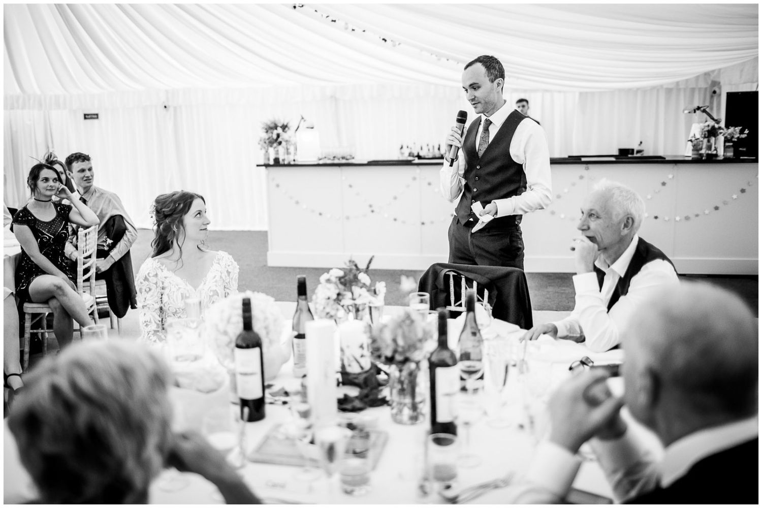 Black and white candid shots of guests enjoying a wedding reception dinner in an elegant marquee setting.