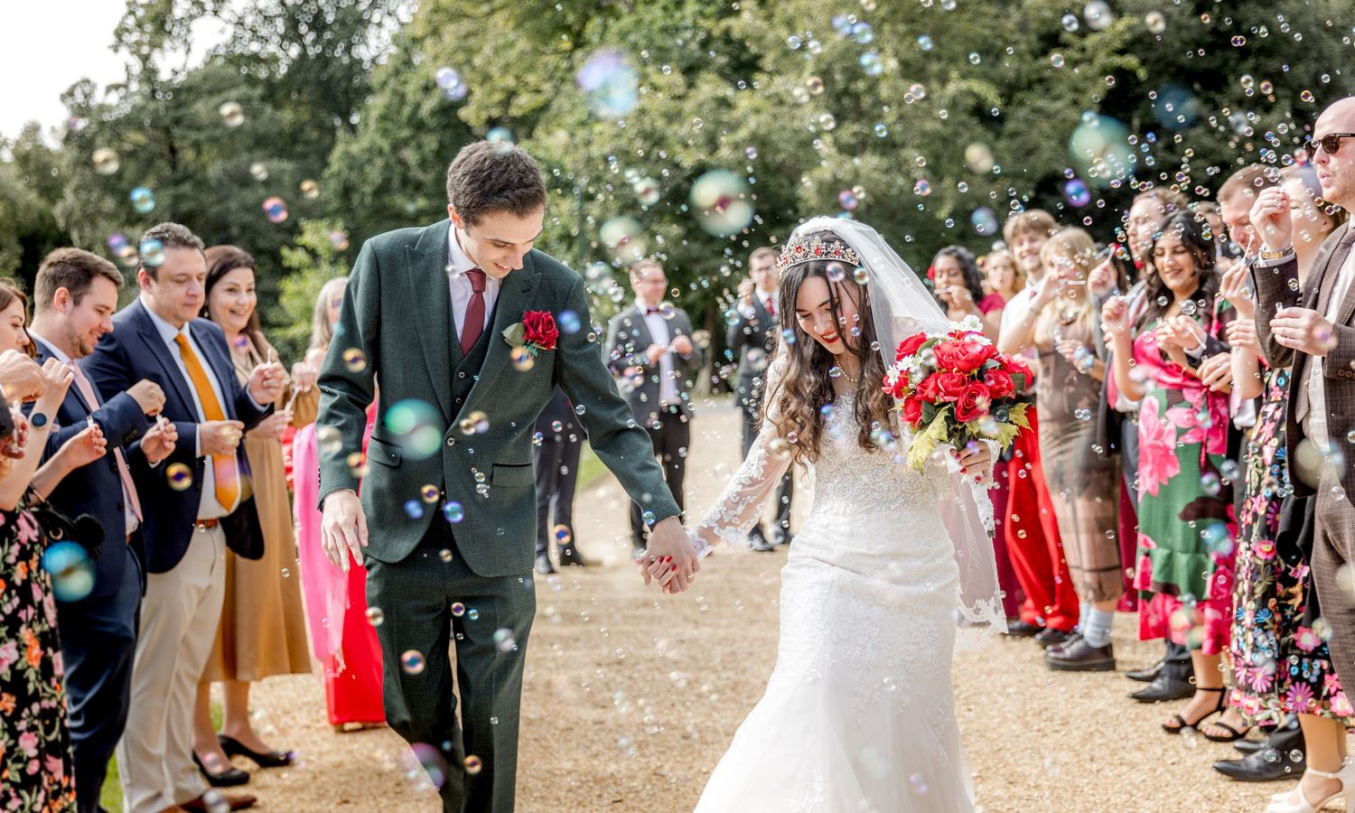 Wedding guests line up outside to celebrate during a confetti toss in a lush garden setting.