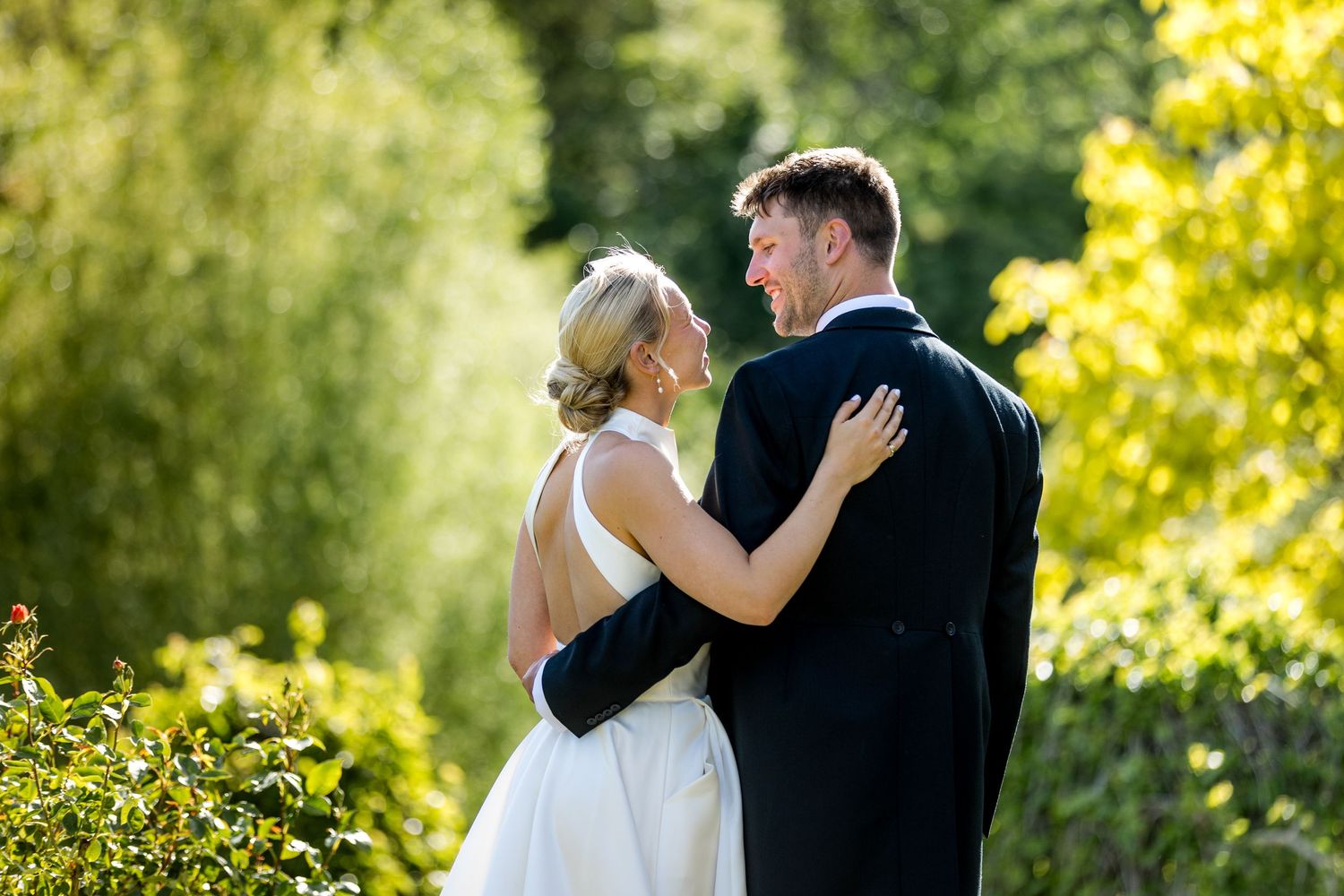 Intimate garden portrait of couple embracing among summer foliage.
