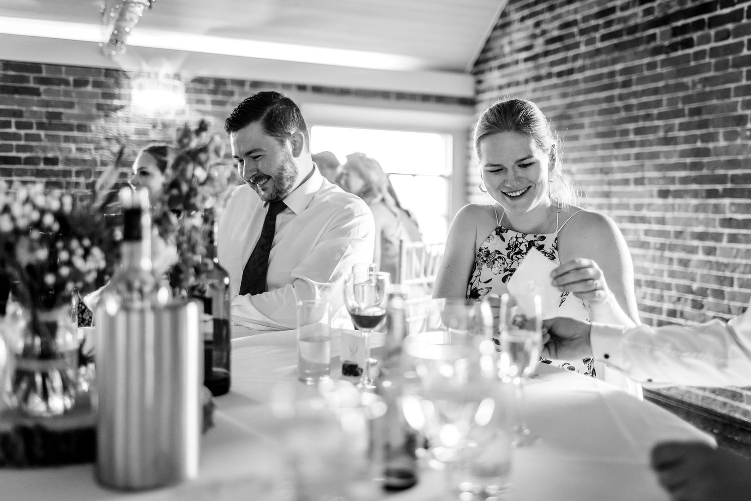 Wedding reception dining scene with natural light streaming through windows onto brick walls.