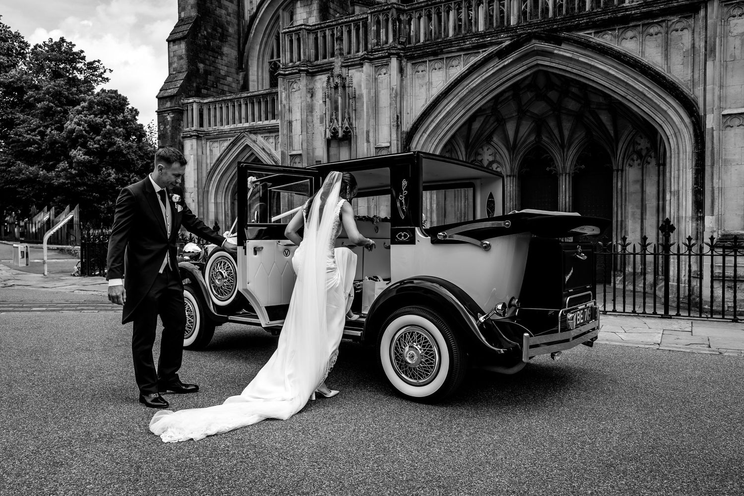 Black and white photos of wedding couple with classic car outside gothic cathedral entrance.