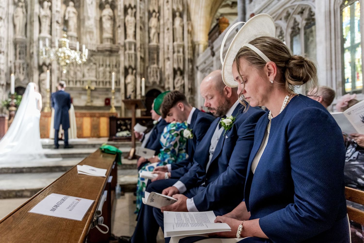 Row of wedding attendees in formal attire seated in historic church pews.