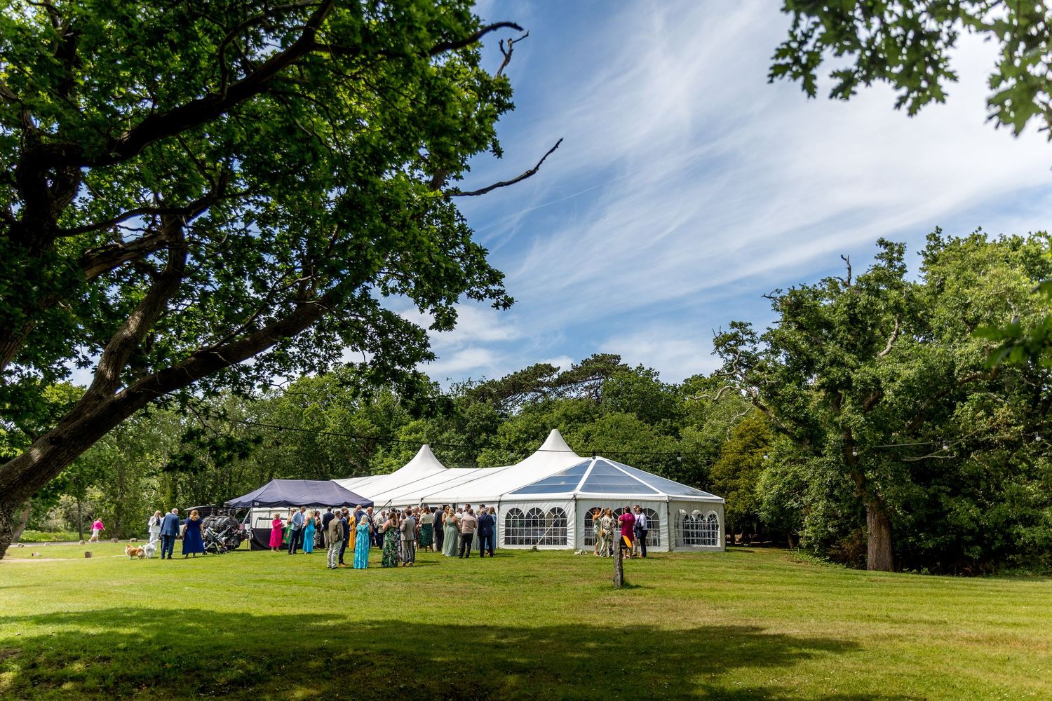 White event tent set up on sprawling green lawn with trees in background.