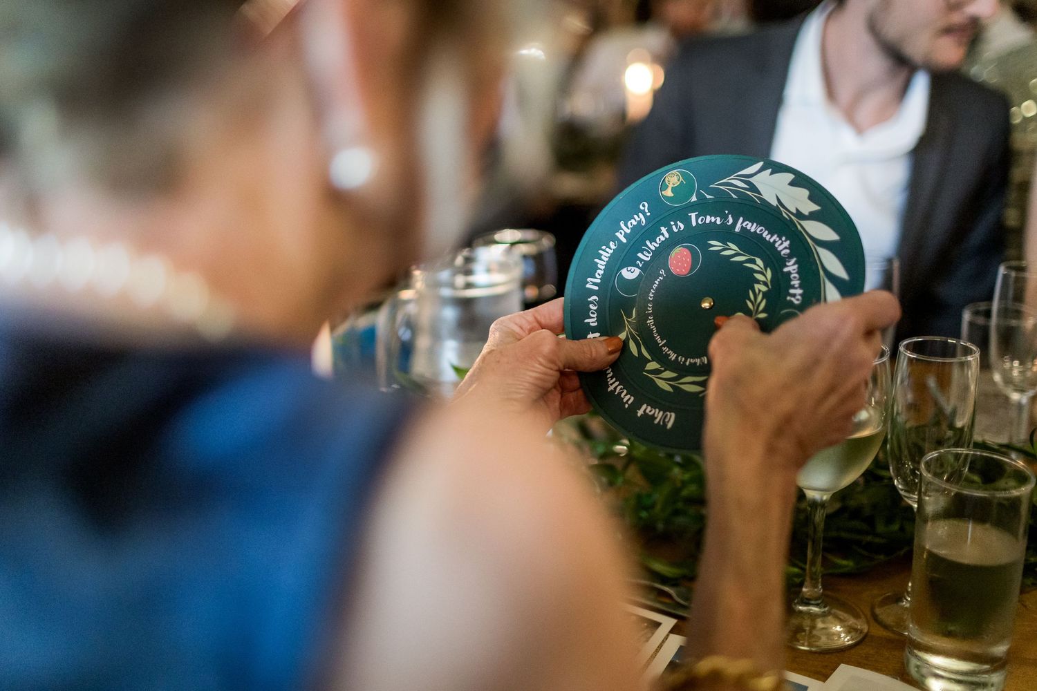 People examining a round green coaster or drink mat at a bar table with beverages visible in the background.