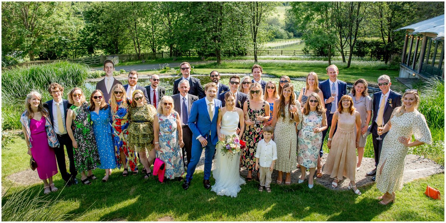 Large group wedding photos taken in a scenic garden setting with natural landscaping.