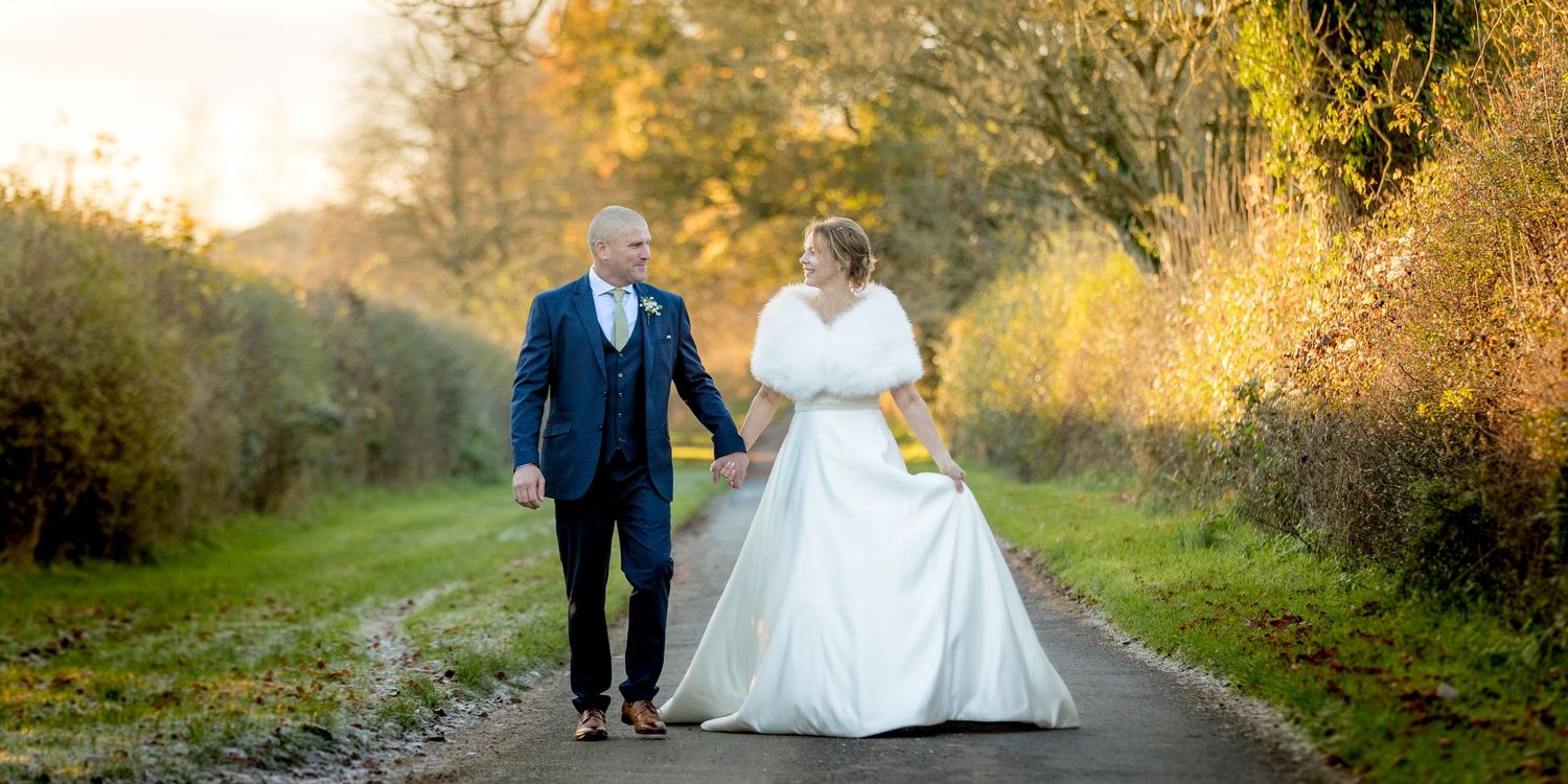 Bride and groom walk along the drive in Autumn light for a wedding portrait photograph at Hampshire's Clock Barn