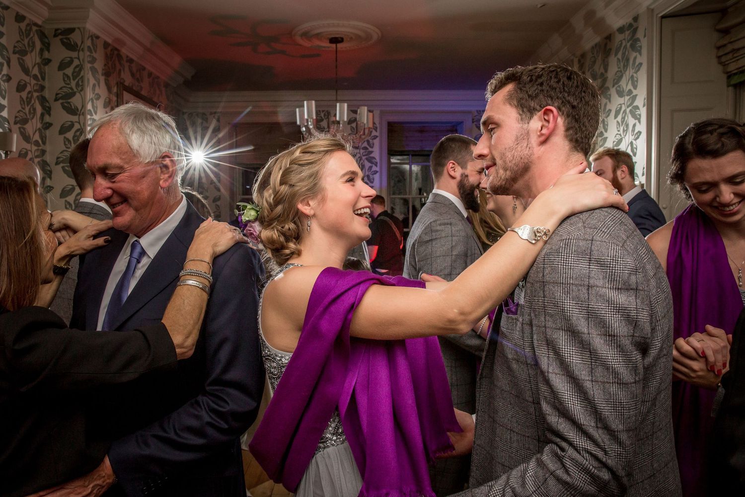 Wedding guests dancing and celebrating at an evening reception in an ornate room.