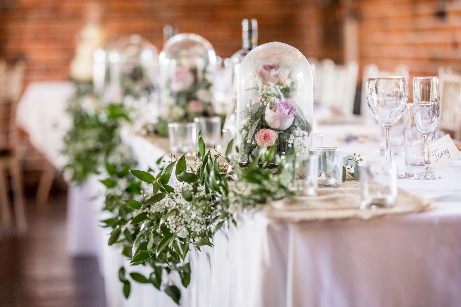 Elegant wedding reception table decorated with glass domes, fresh flowers and greenery garlands.