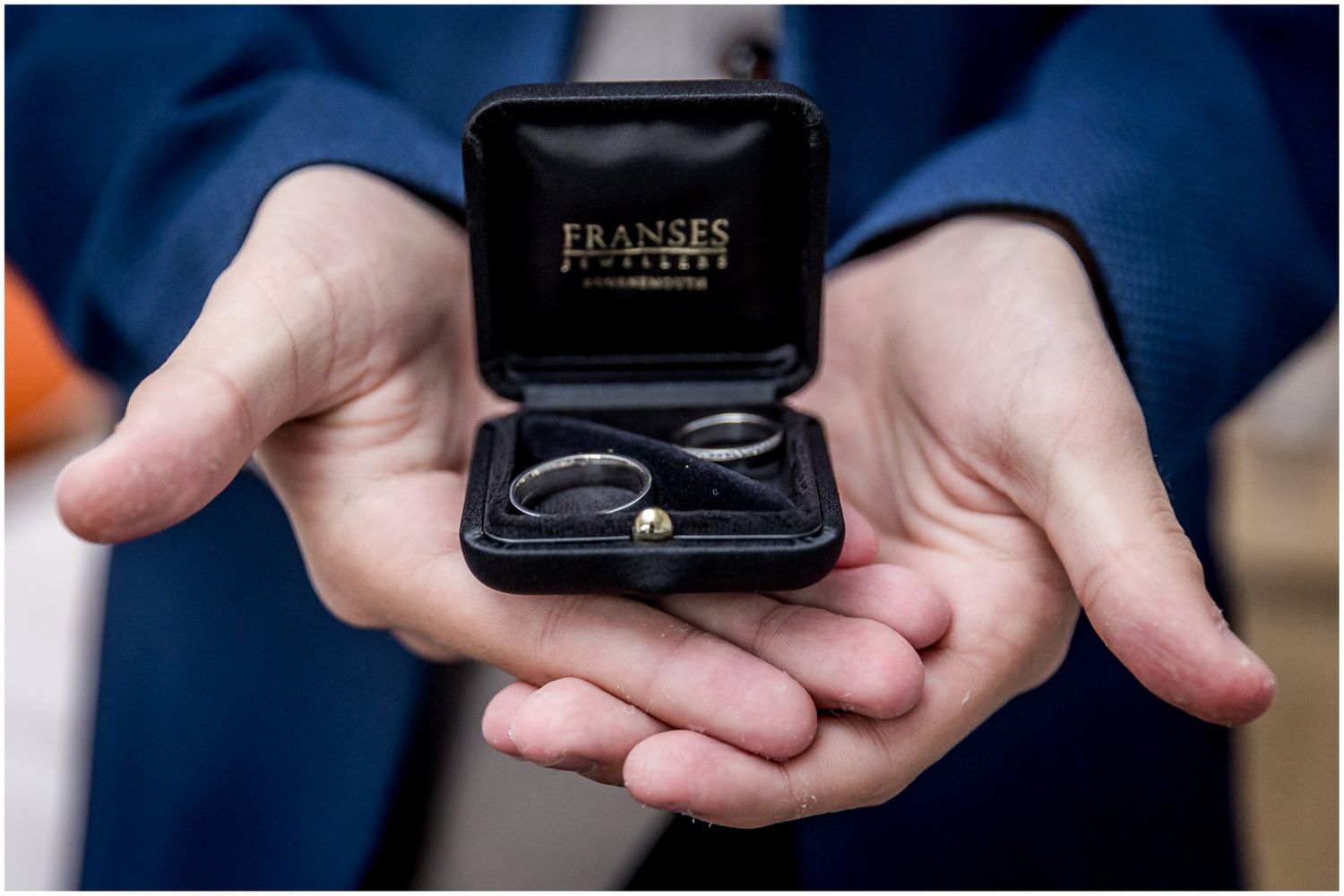 Close-up of hands holding an open ring box from Fransses jewelers.