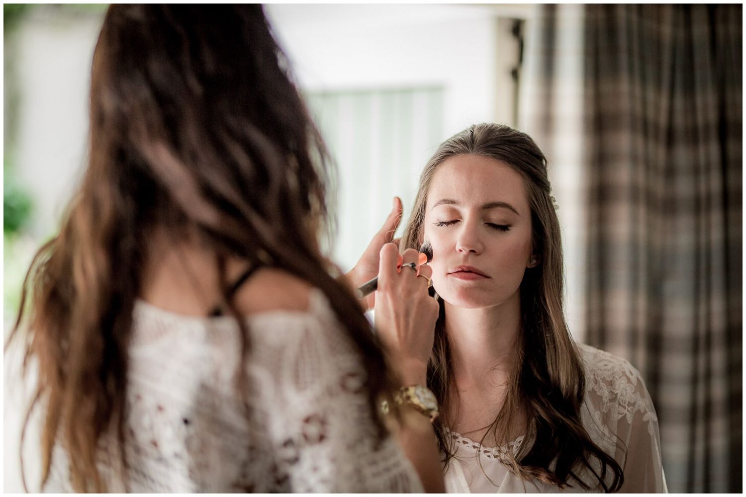 A bride in a white dress poses near a window with natural light streaming in during a wedding photoshoot.