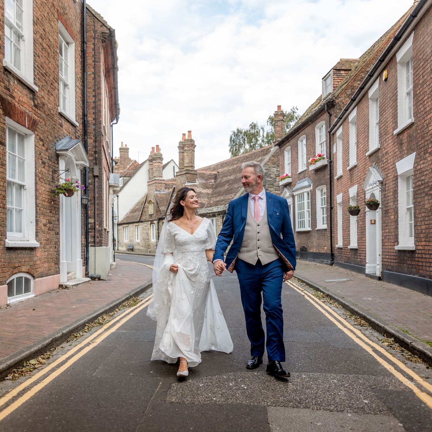 Wedding portraits on a sloping cobblestone street surrounded by historic brick buildings.