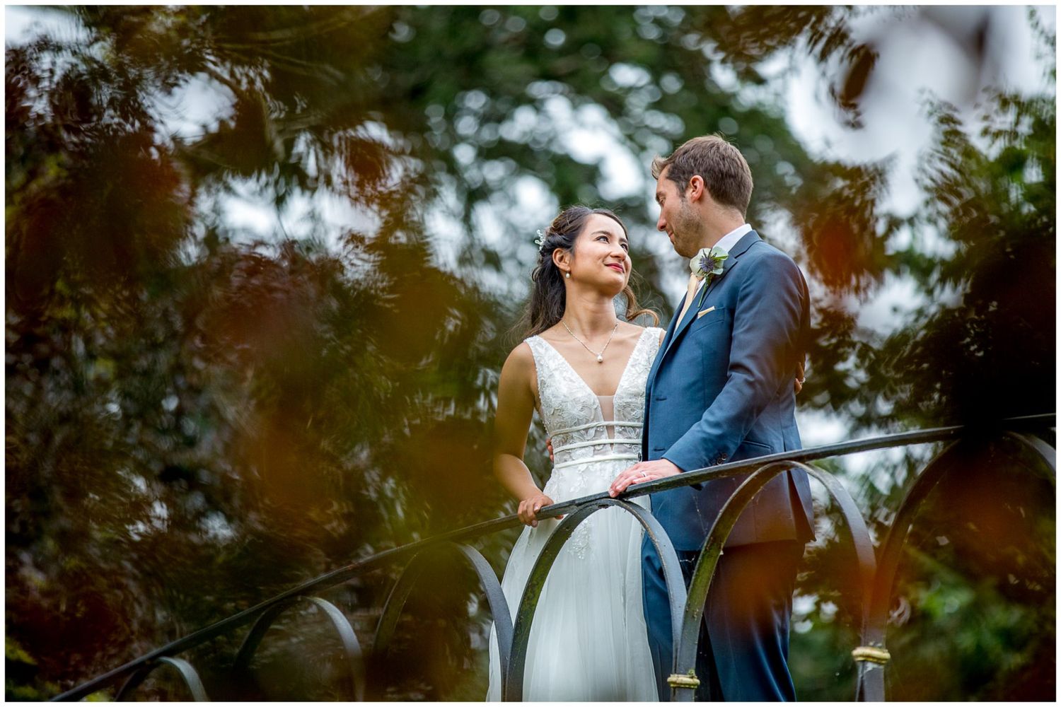 Intimate wedding portrait of couple on ornate bridge surrounded by lush greenery.