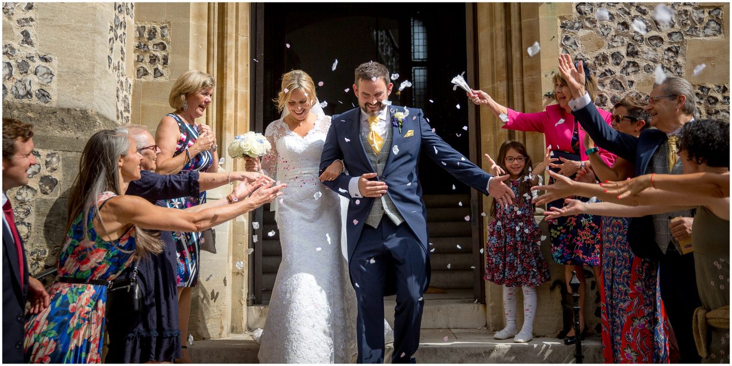 Wedding guests shower newlyweds with confetti as they exit a church building in celebration.