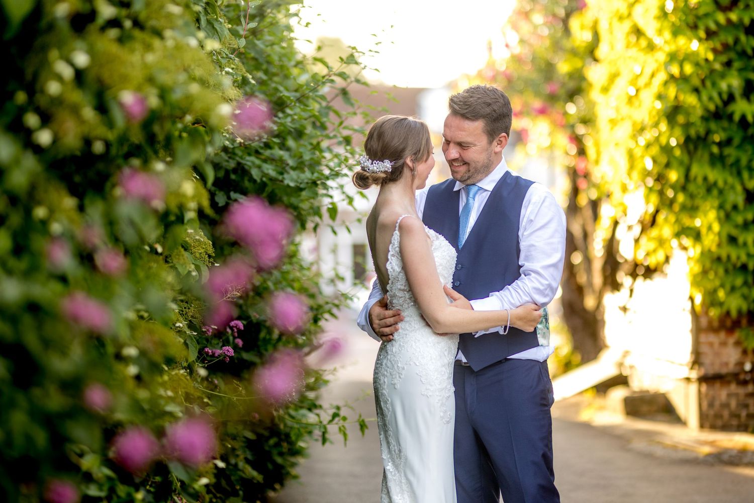 A romantic moment captured in a sunlit garden with pink flowers in the foreground.