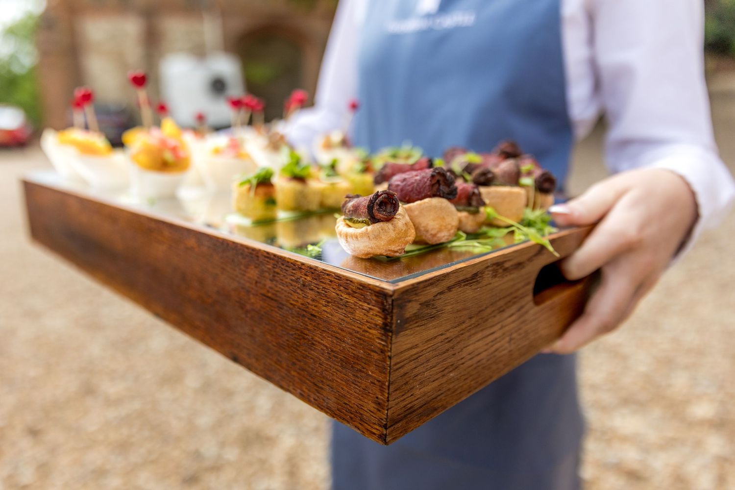 Wooden serving trays with appetizers being presented at an outdoor wedding reception.