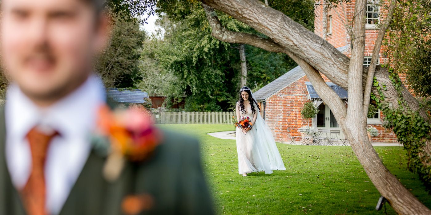 Couple shares tender moment in garden setting with brick building in background.