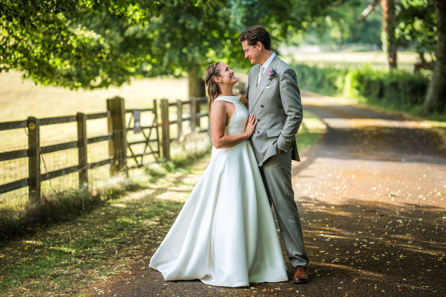 Romantic wedding portraits taken on a tree-lined path with wooden fencing.
