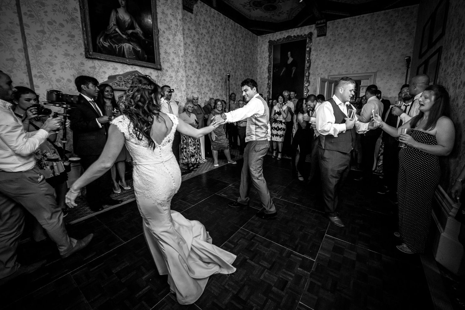 Black and white photo of wedding reception dance party with guests dancing in an elegant indoor venue.