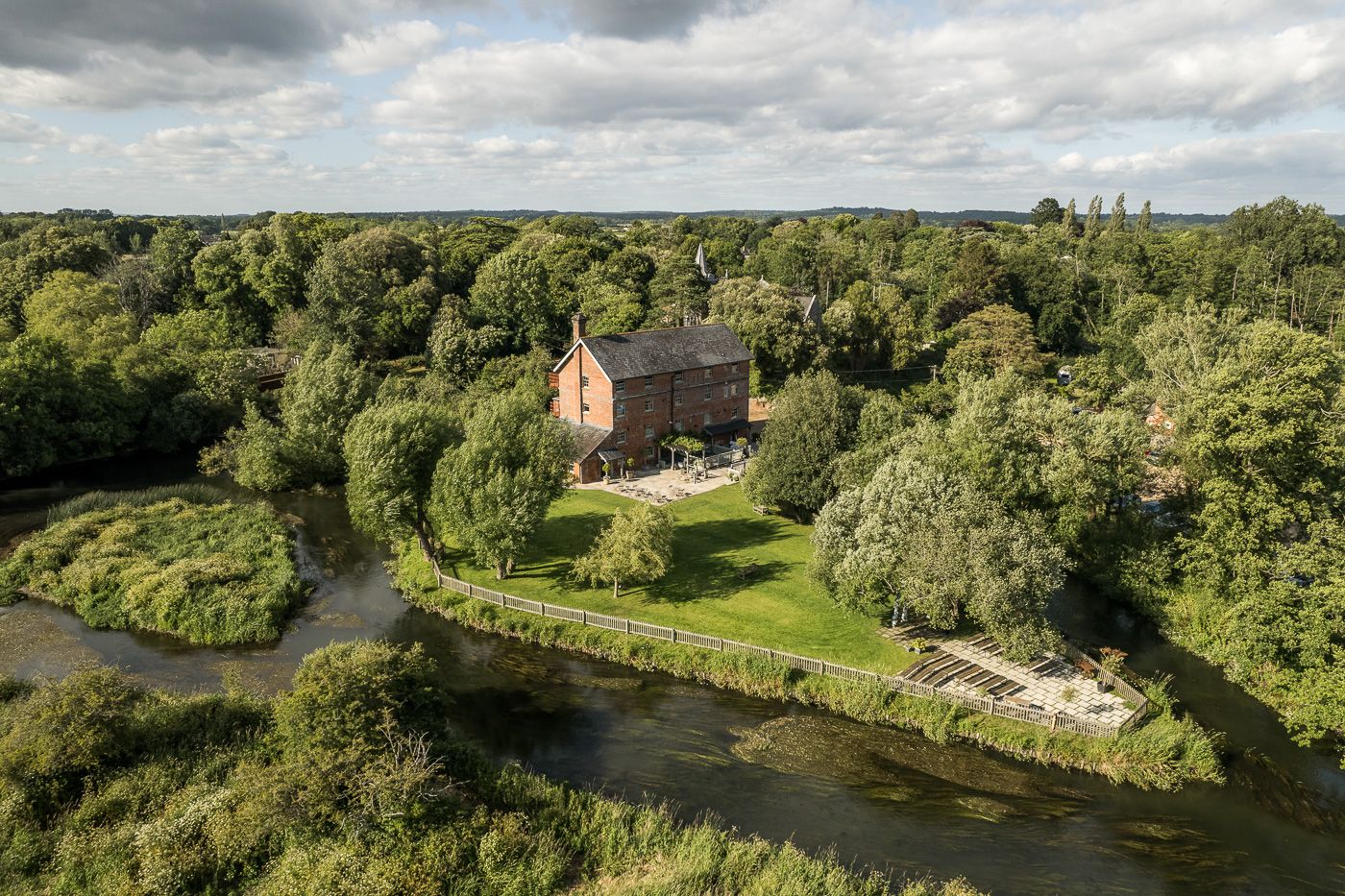 Aerial view of a historic stone building nestled among trees along a winding river.