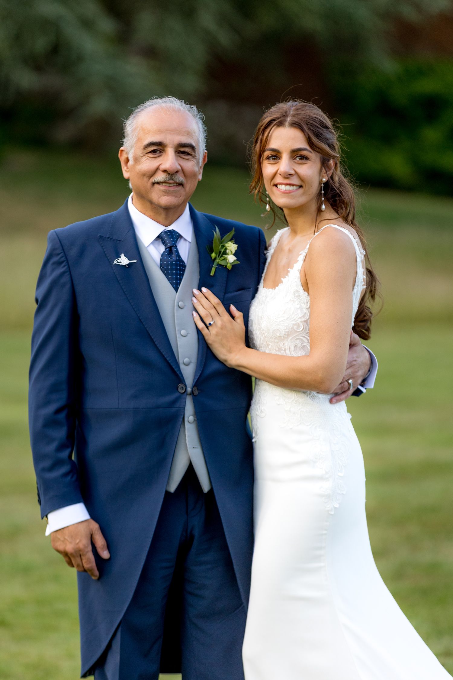 Wedding couple poses together outdoors in formal attire against a green lawn background.