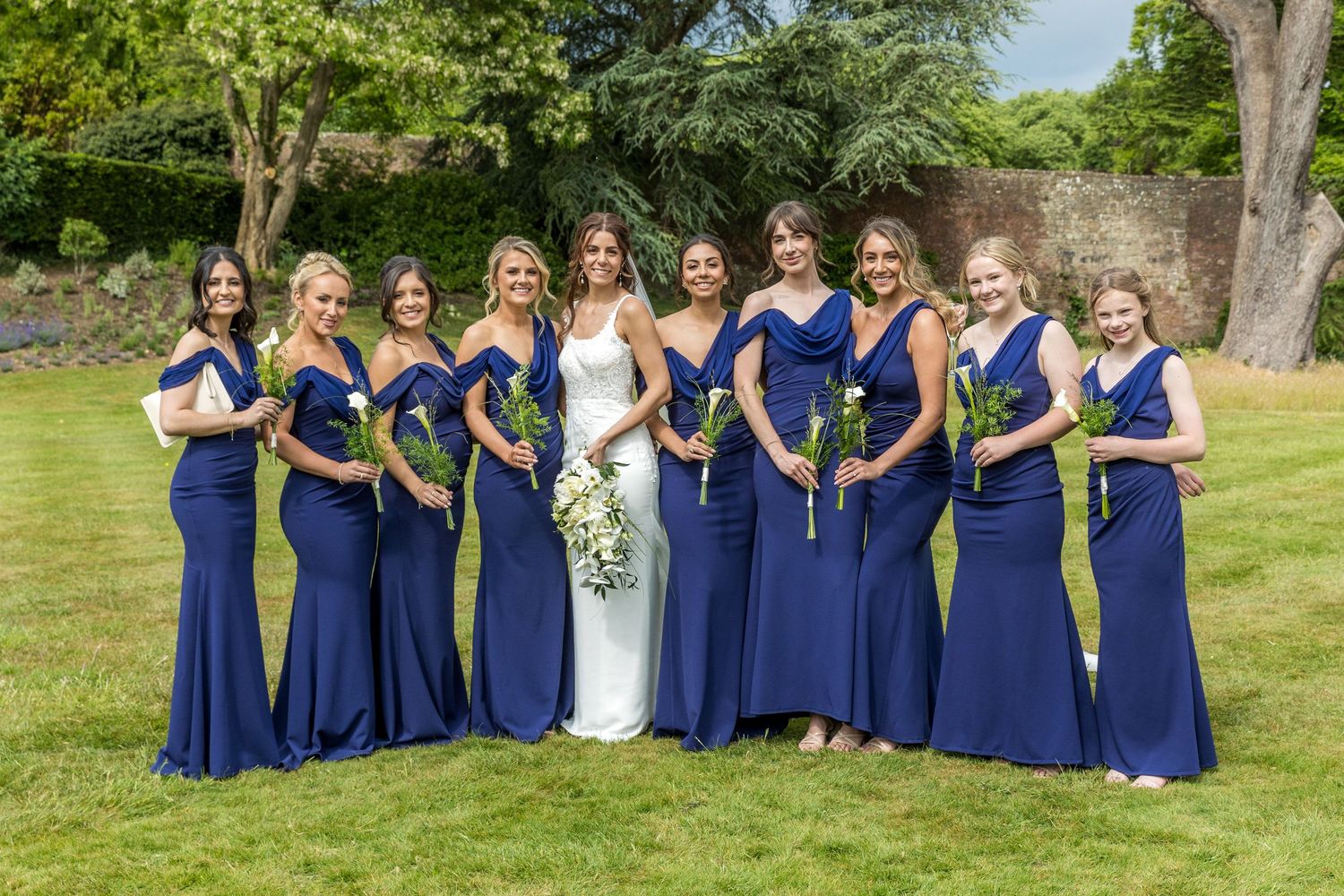 Wedding party in navy blue dresses poses together on a sunny lawn for formal group photos.