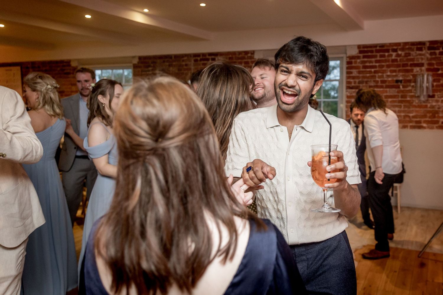 Guests enjoying themselves at a lively wedding reception with brick wall backdrop.