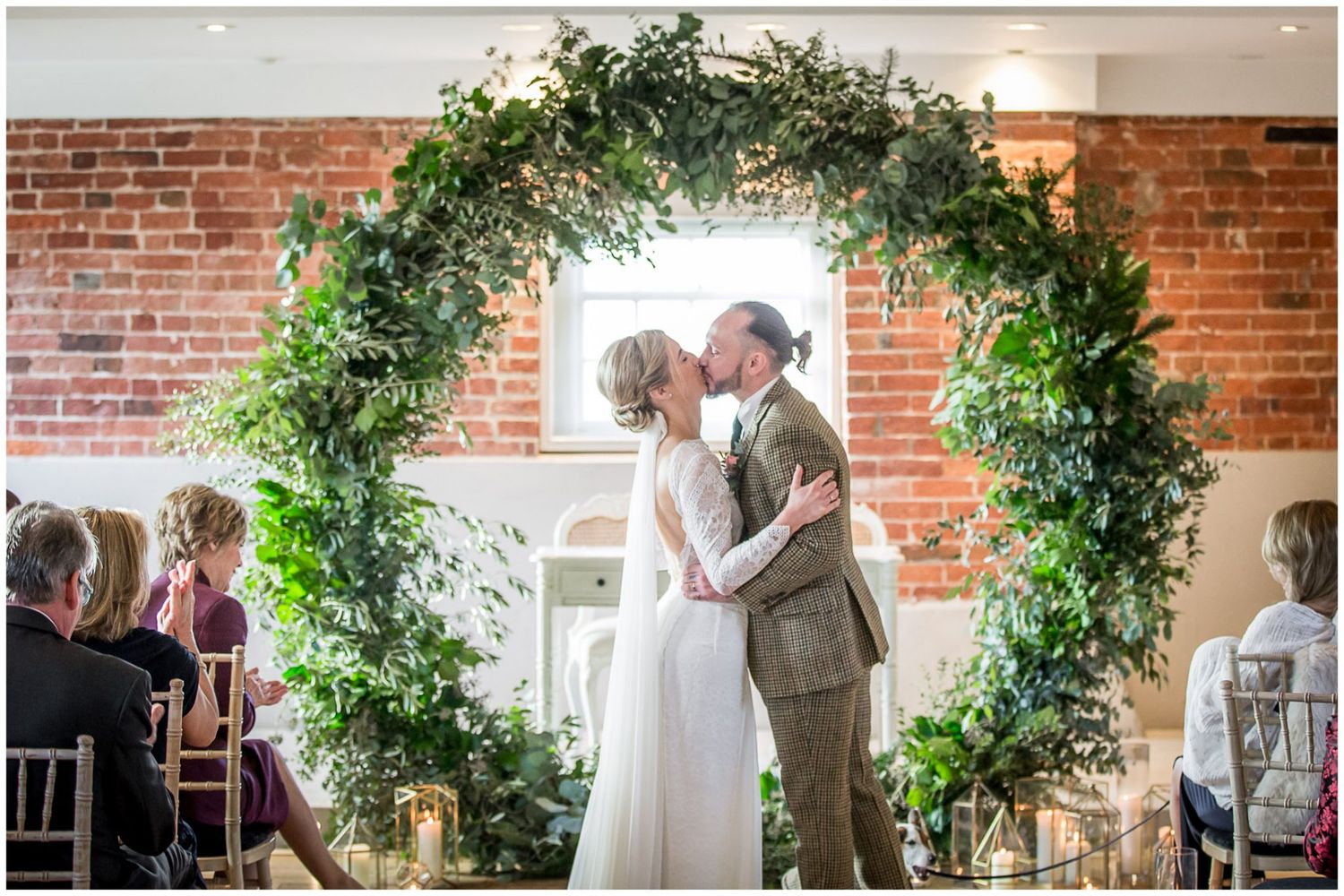 Wedding ceremony space with lush greenery arch and exposed brick interior.