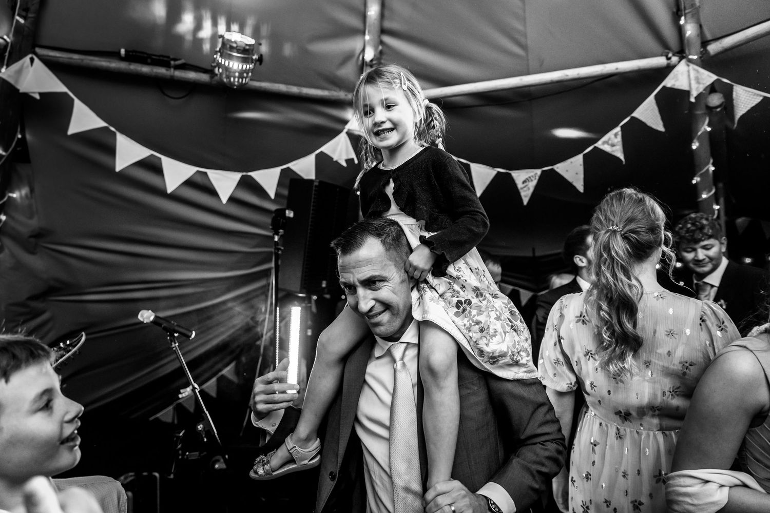 Black and white photo of party guests dancing beneath triangular bunting flags at an indoor celebration.