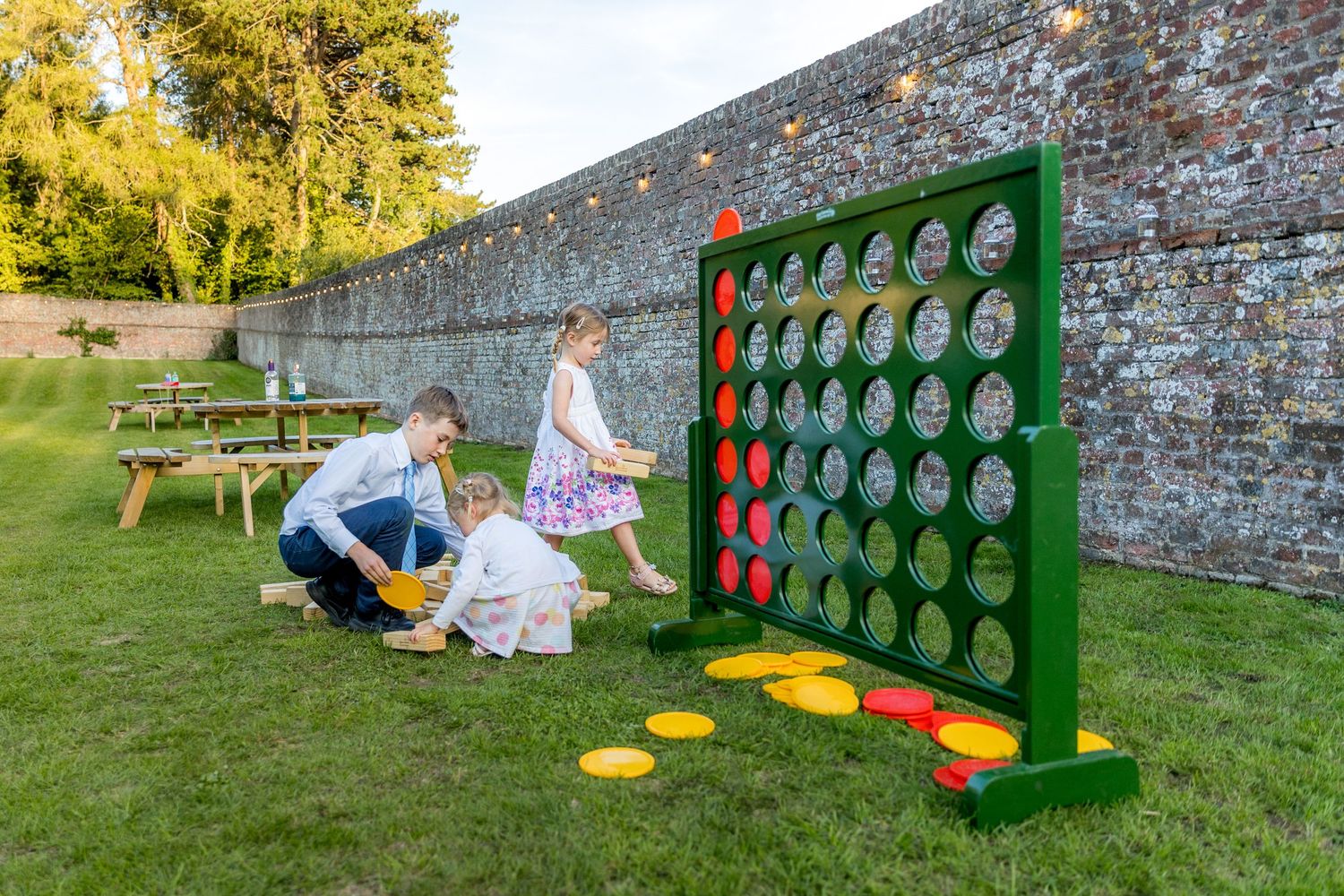 Giant Connect Four game set up on a lawn against a stone wall at an outdoor event.