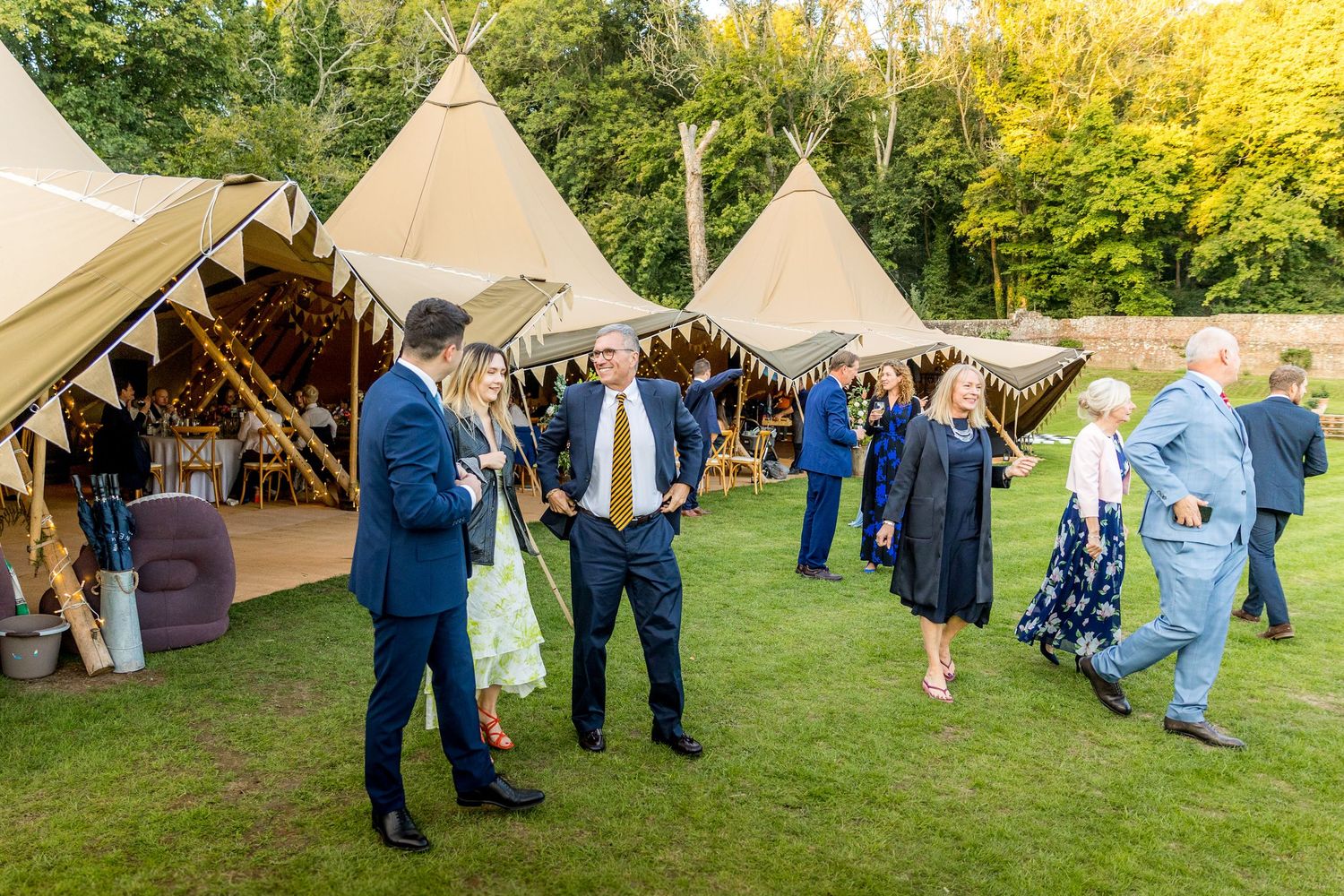 Wedding celebration with guests in blue attire gathering near white reception tents.
