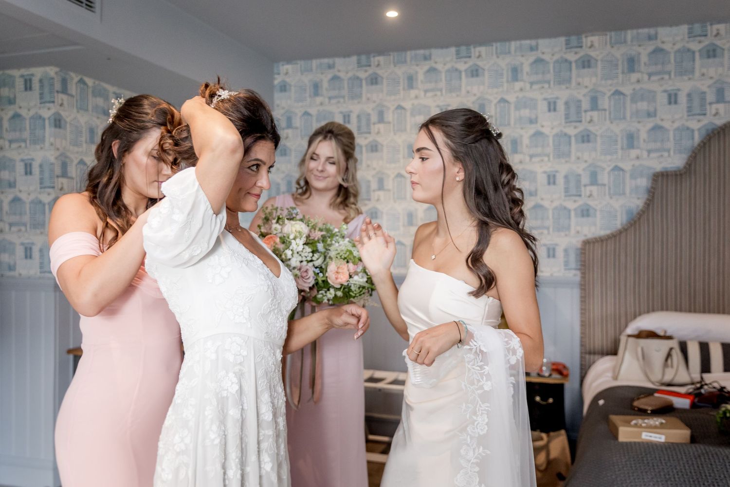 Wedding party getting ready in room with blue patterned wallpaper.