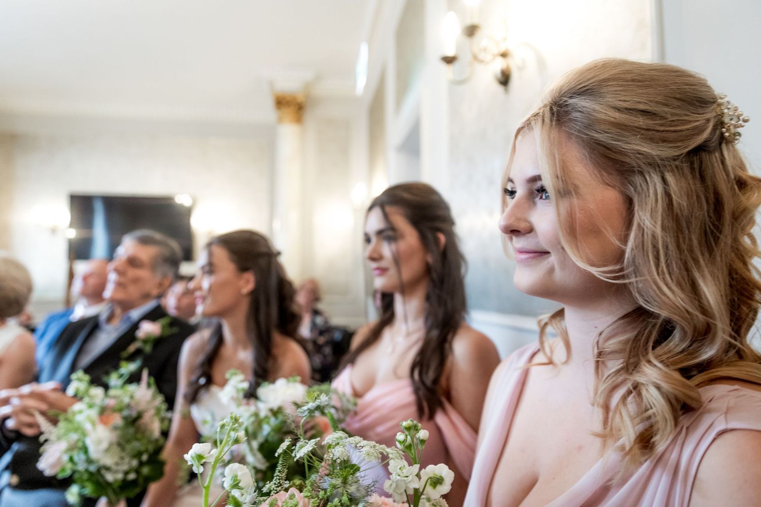 Wedding attendees seated in a row with floral bouquets and elegant decor.