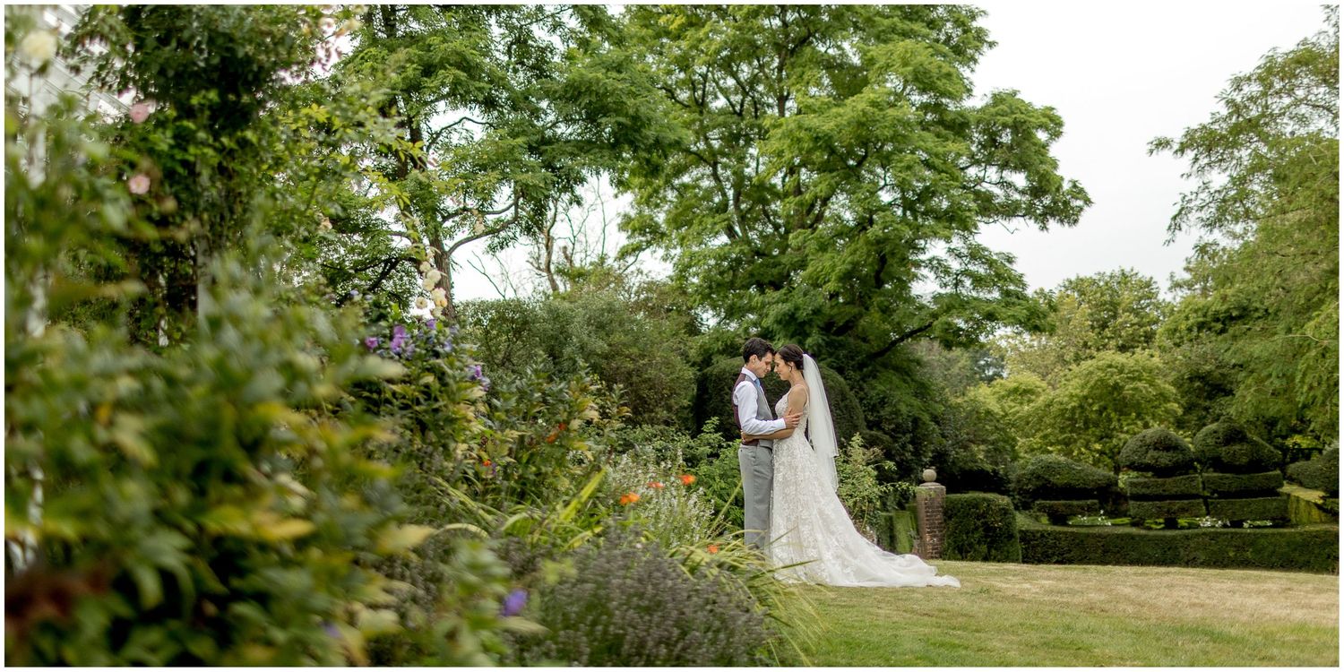 Wedding couple shares tender moments in a lush garden setting surrounded by green trees.