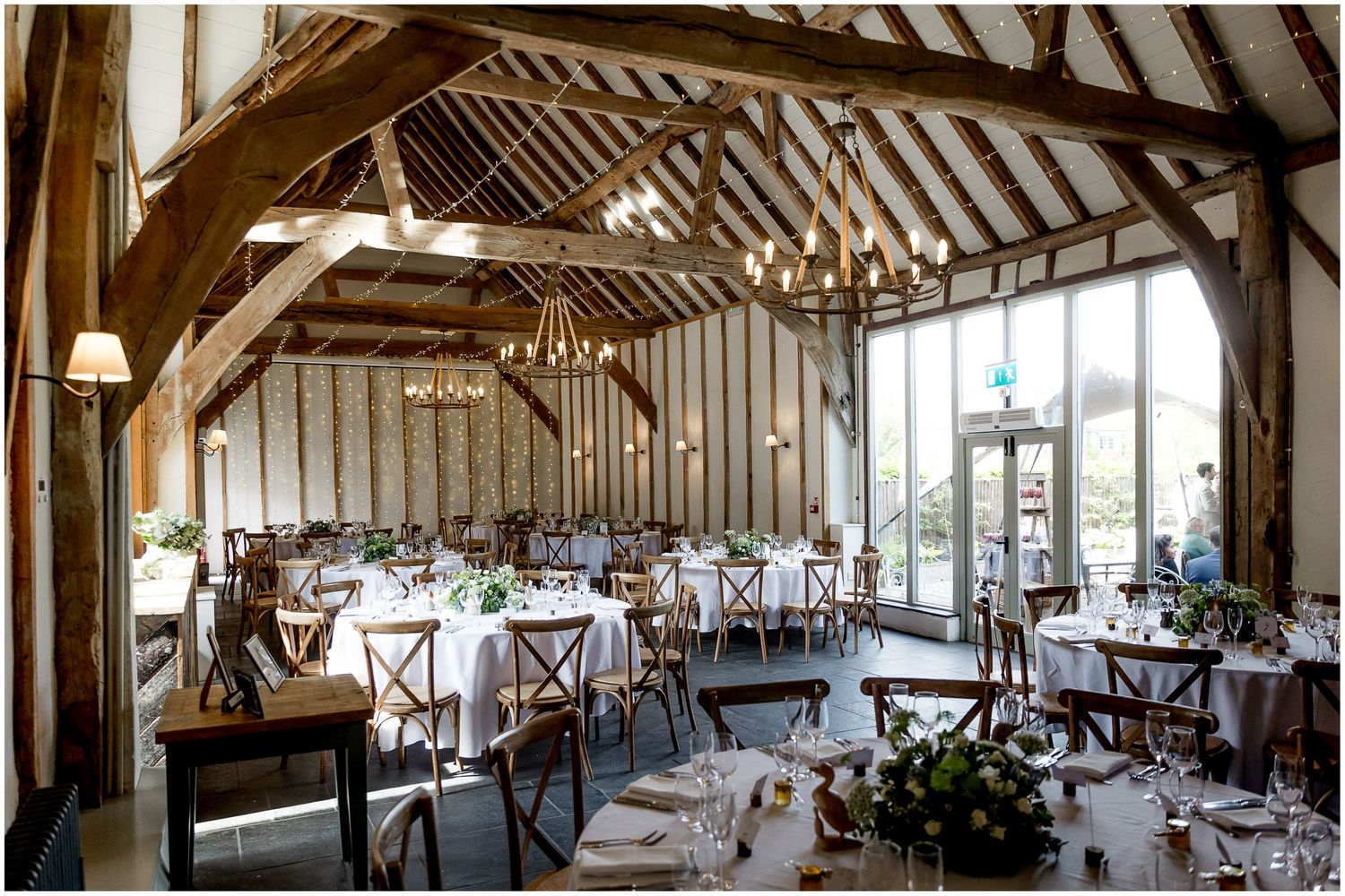 Rustic barn venue set up for a wedding reception with exposed wooden beams and round tables.