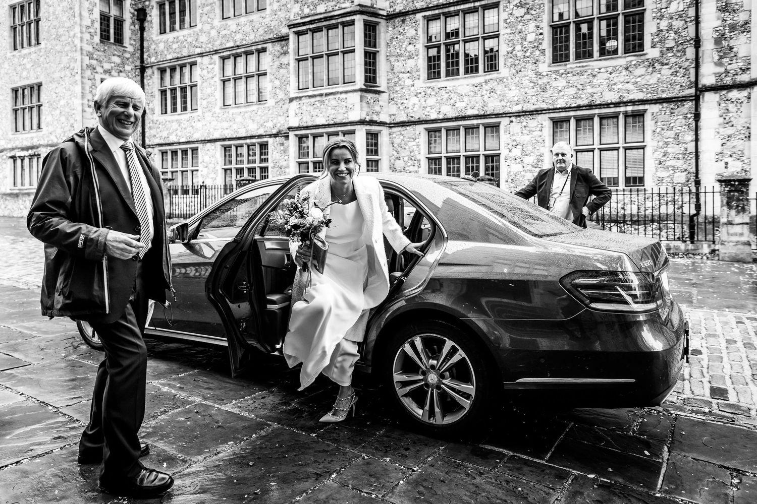 A luxury car arrives at a historic stone building on a wedding day.