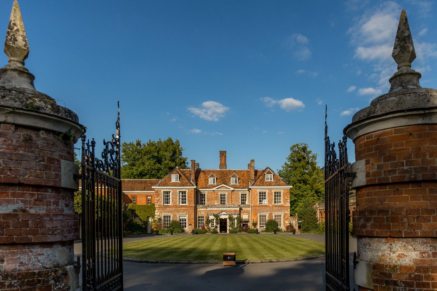 Grand brick mansion with ornate gates and landscaping viewed from multiple angles in daytime.