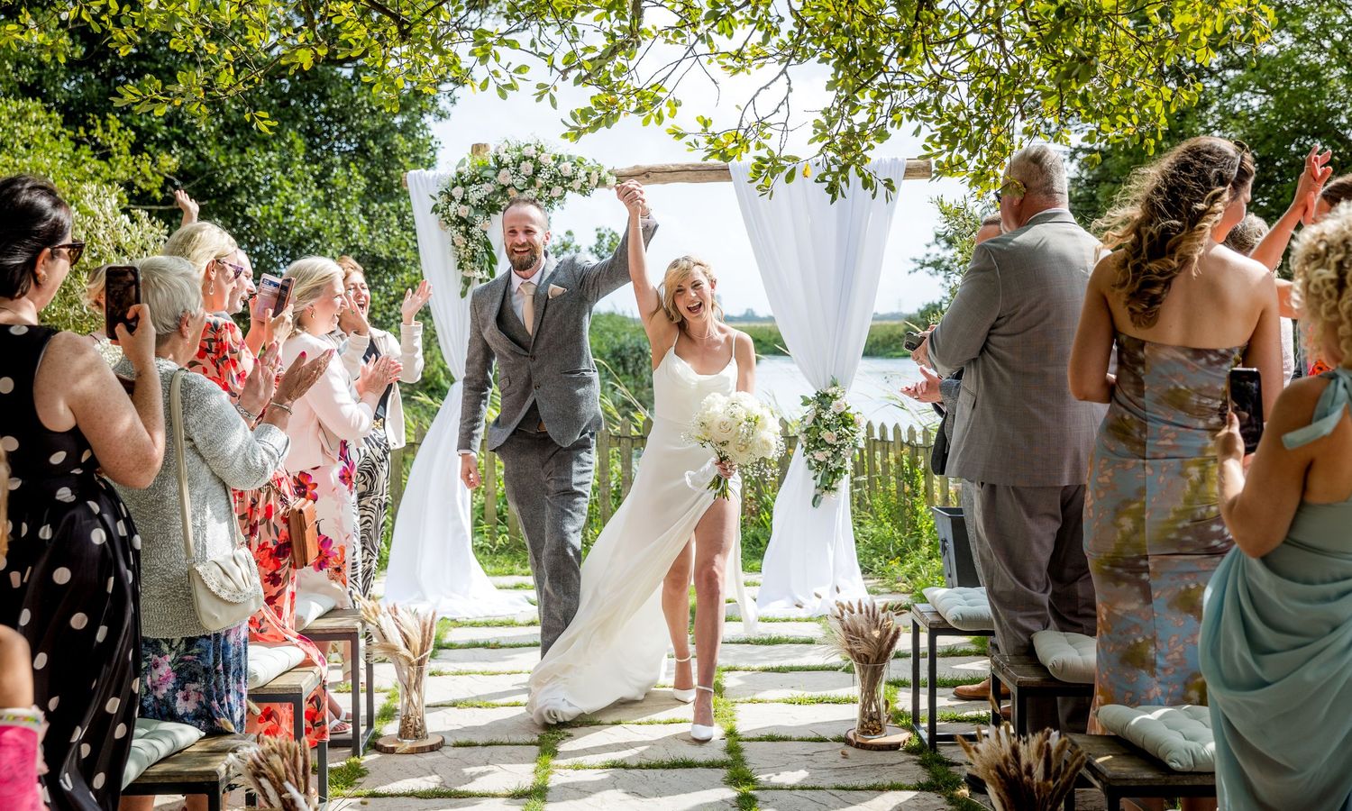 Wedding guests celebrate during an outdoor garden reception with string lights and white decor.