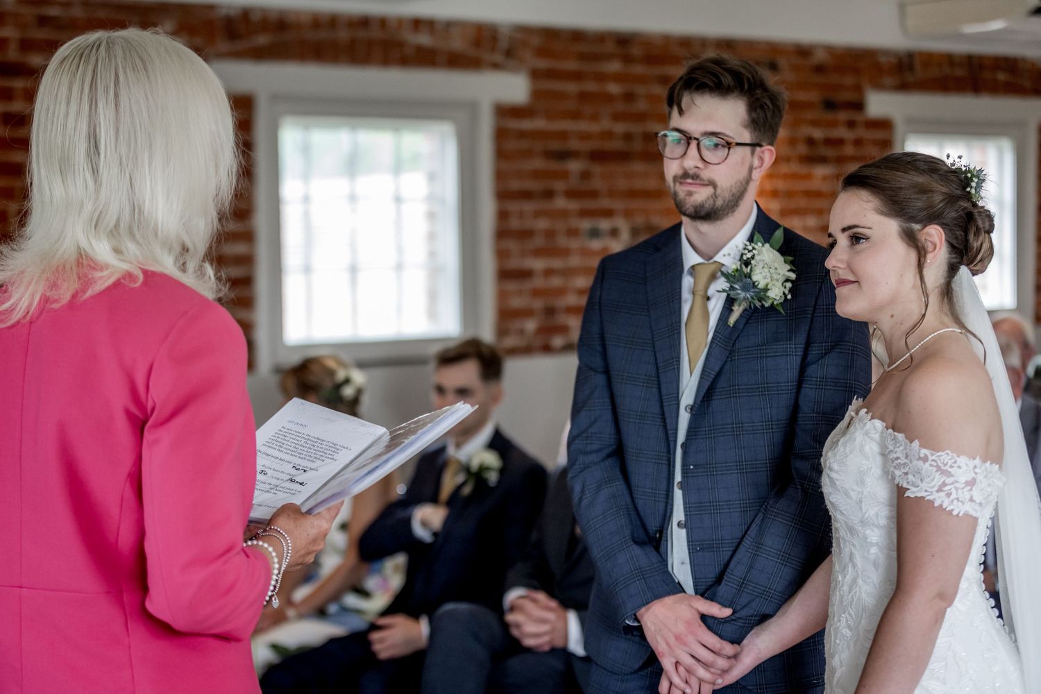 Wedding ceremony participants gathered in a bright industrial-style room with brick walls.