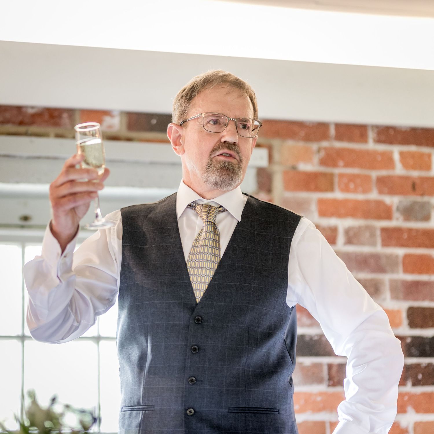 Wedding guests raising glasses for a toast in a brick-walled reception venue.