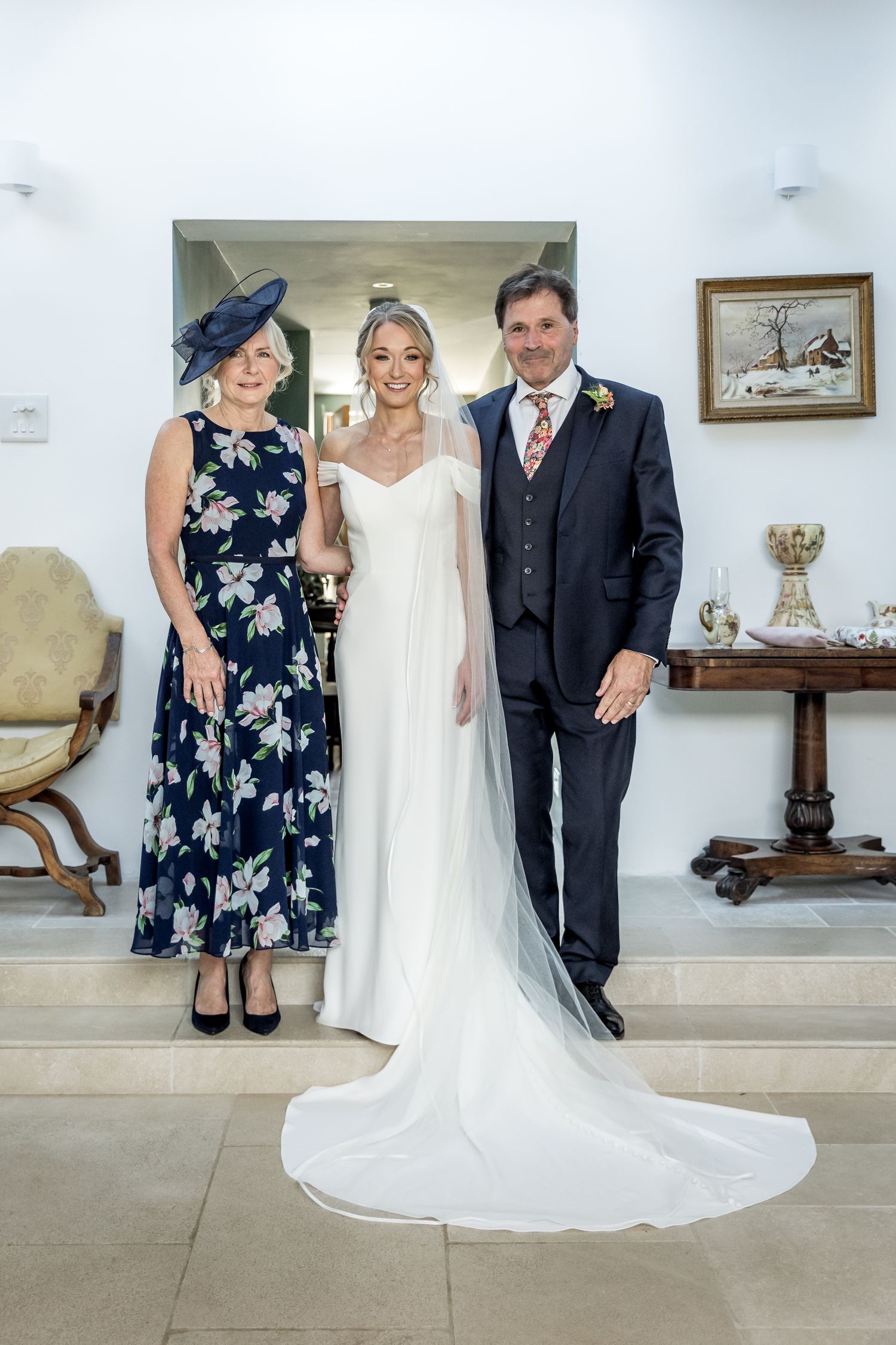 A wedding party poses in formal attire against a white wall with elegant decor.