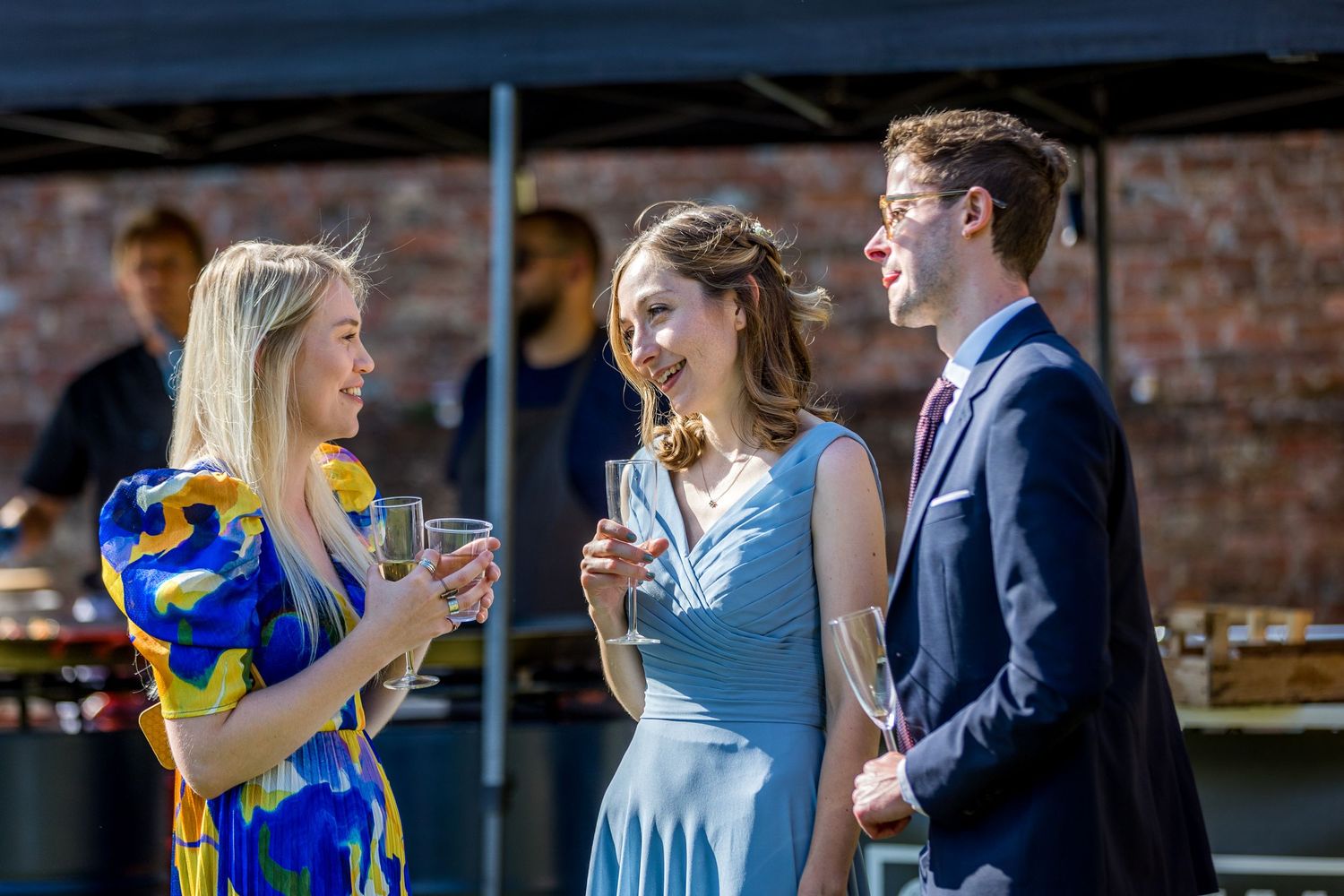 Guests in formal attire gather for drinks and conversation at an outdoor event.