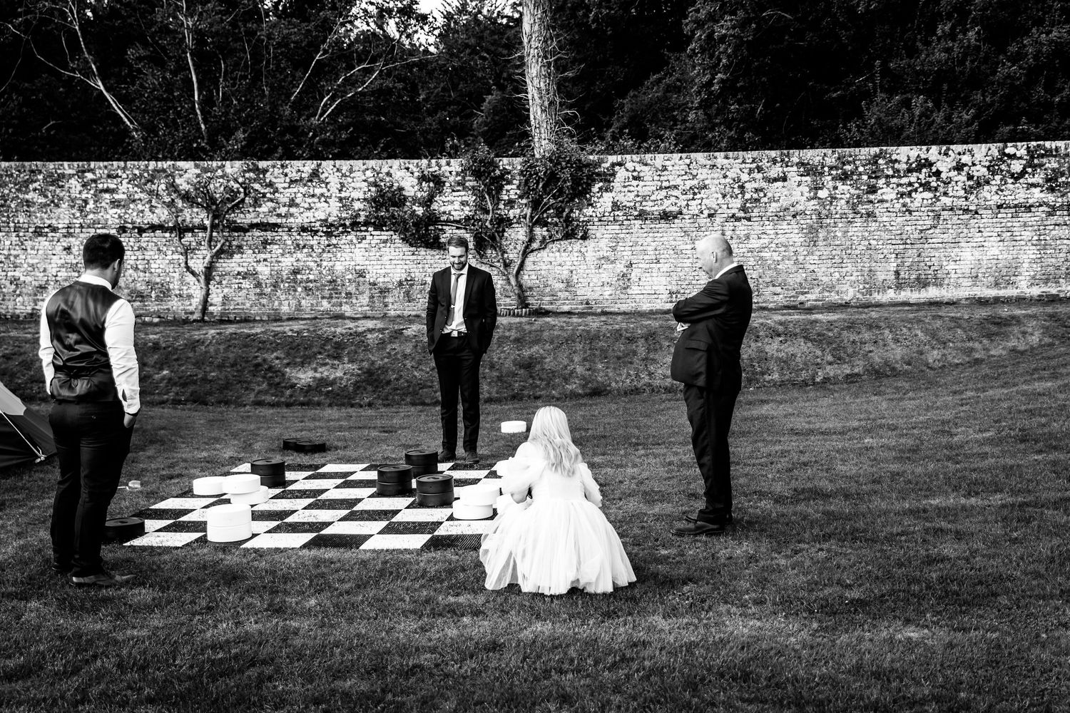Black and white photo of people playing giant checkers on a lawn during a wedding celebration.