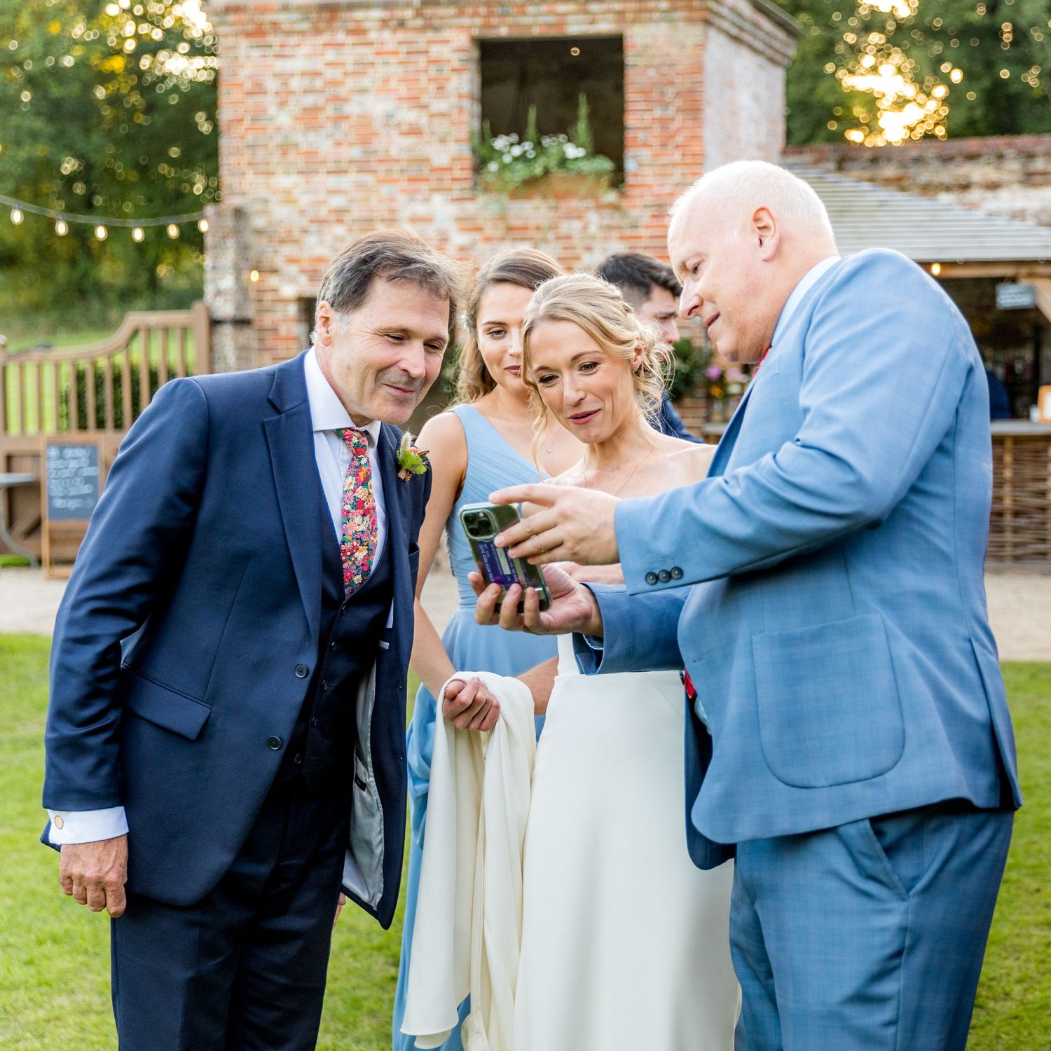 Wedding guests looking at mobile phones during outdoor reception by brick wall.