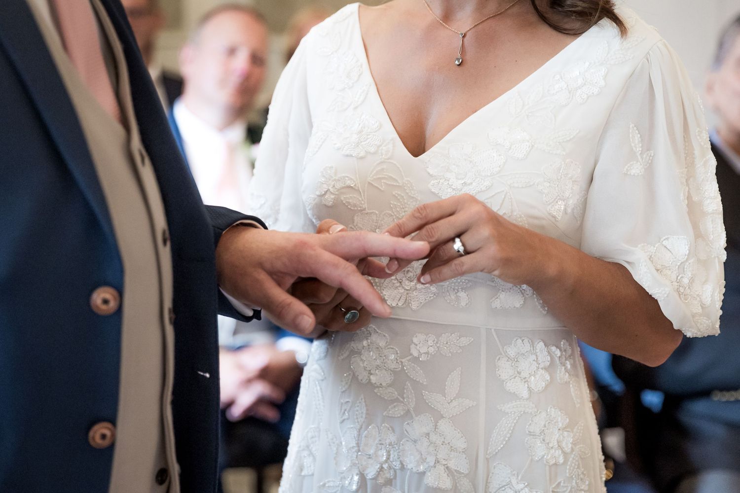 Close up of hands exchanging wedding rings with a detailed lace dress visible.