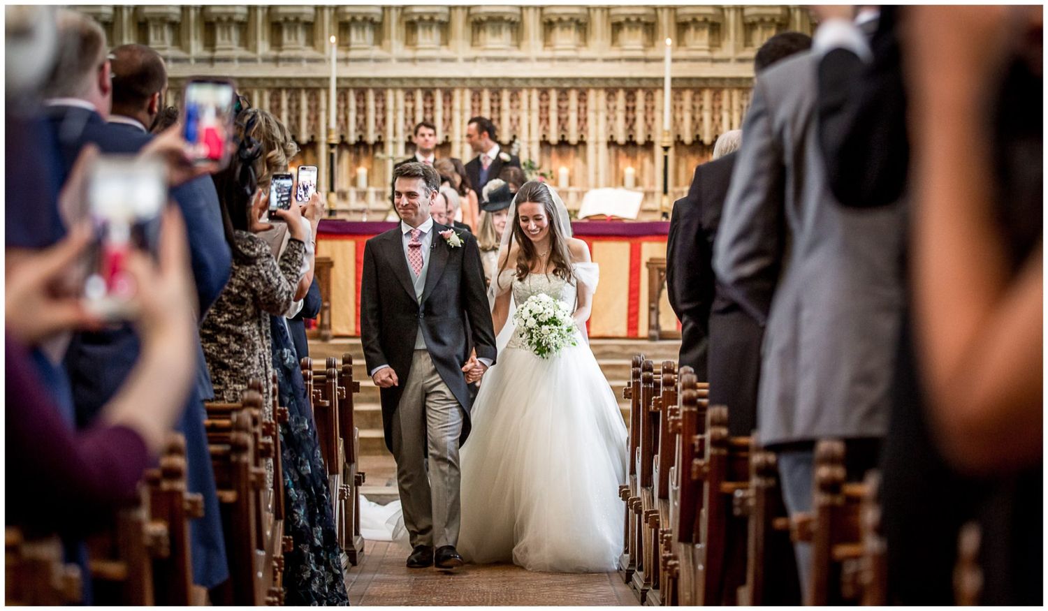 A wedding ceremony takes place inside an ornate cathedral with high vaulted ceilings and decorative stone columns.